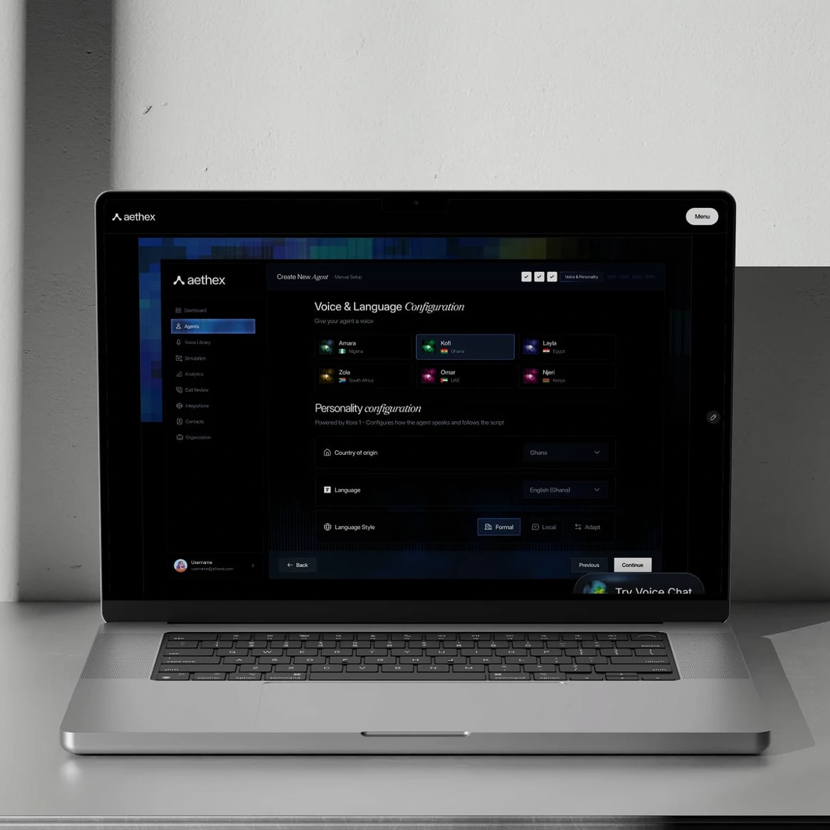 aethex website: Laptop on a steel desk against a light wall, showing the Aethex agent builder: Voice & Language configuration with regional voices