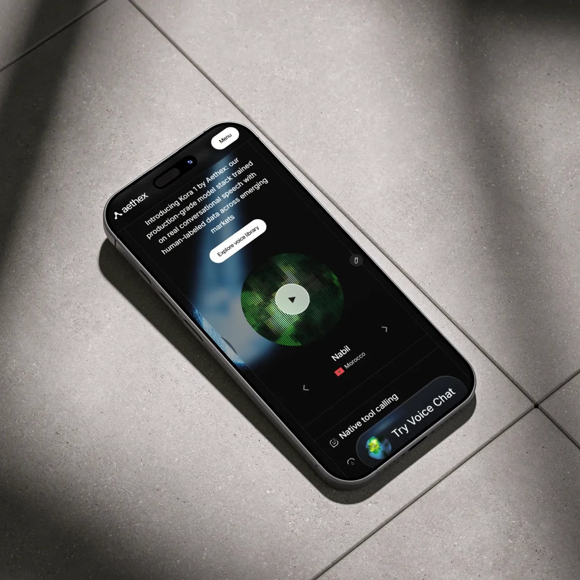 aethex website: Phone on a tiled floor showing the Aethex mobile site: Kora 1 introduction and the voice library player (Nabil, Morocco)