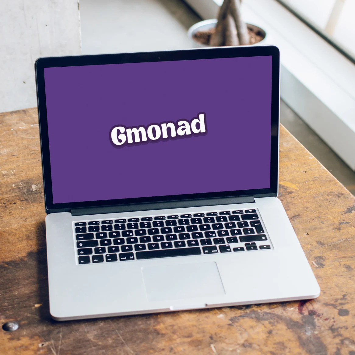 GMONAD website: Laptop on a wooden desk showing the Gmonad wordmark