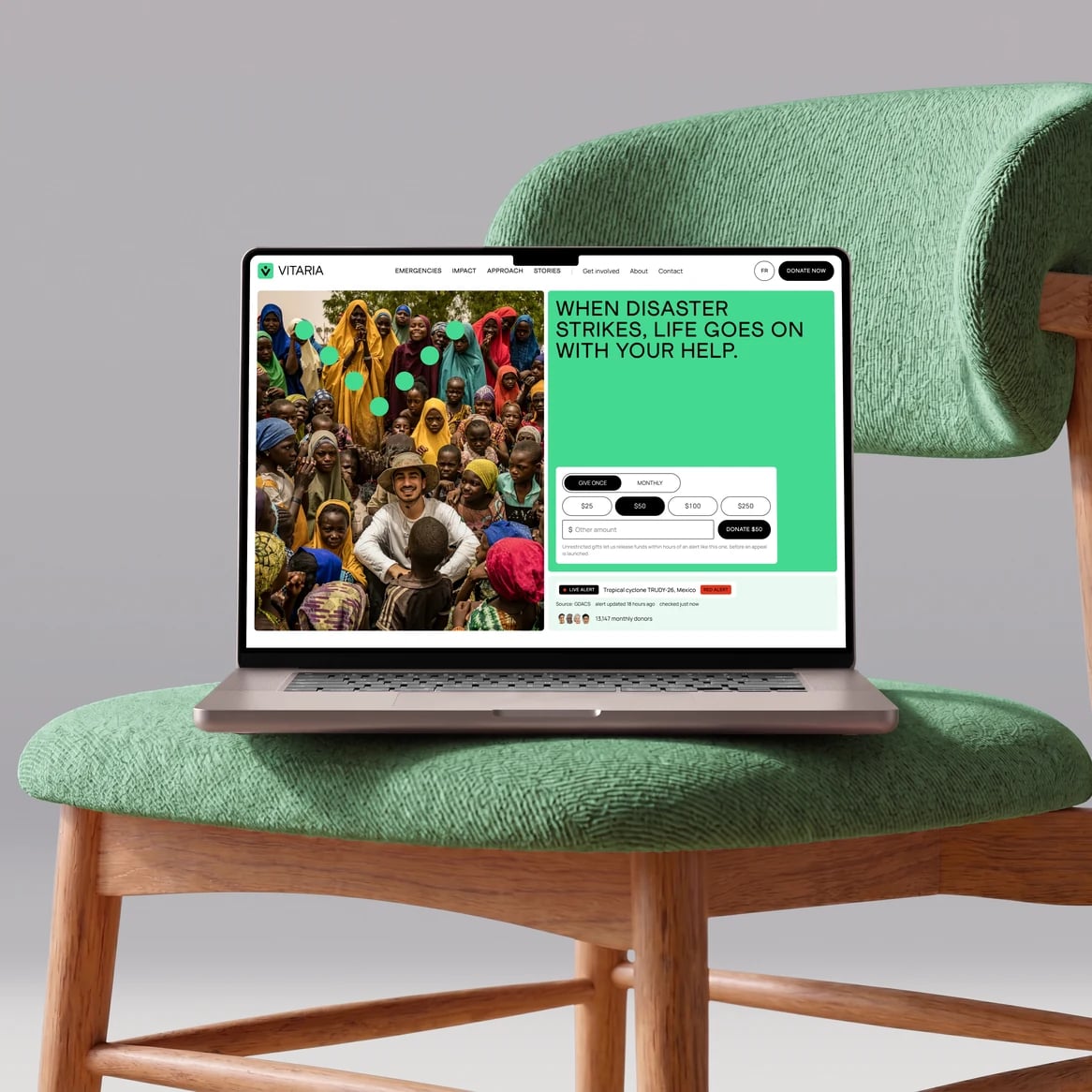 Vitaria website: Laptop on a green bouclé chair showing the Vitaria home page: field photo, headline and the give once or monthly donation form