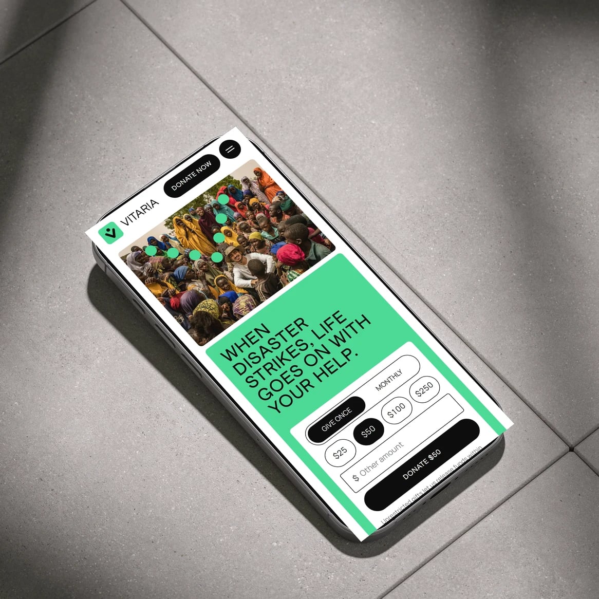 Vitaria website: Phone lying on a concrete floor in diagonal light, showing the Vitaria mobile home page and donation form