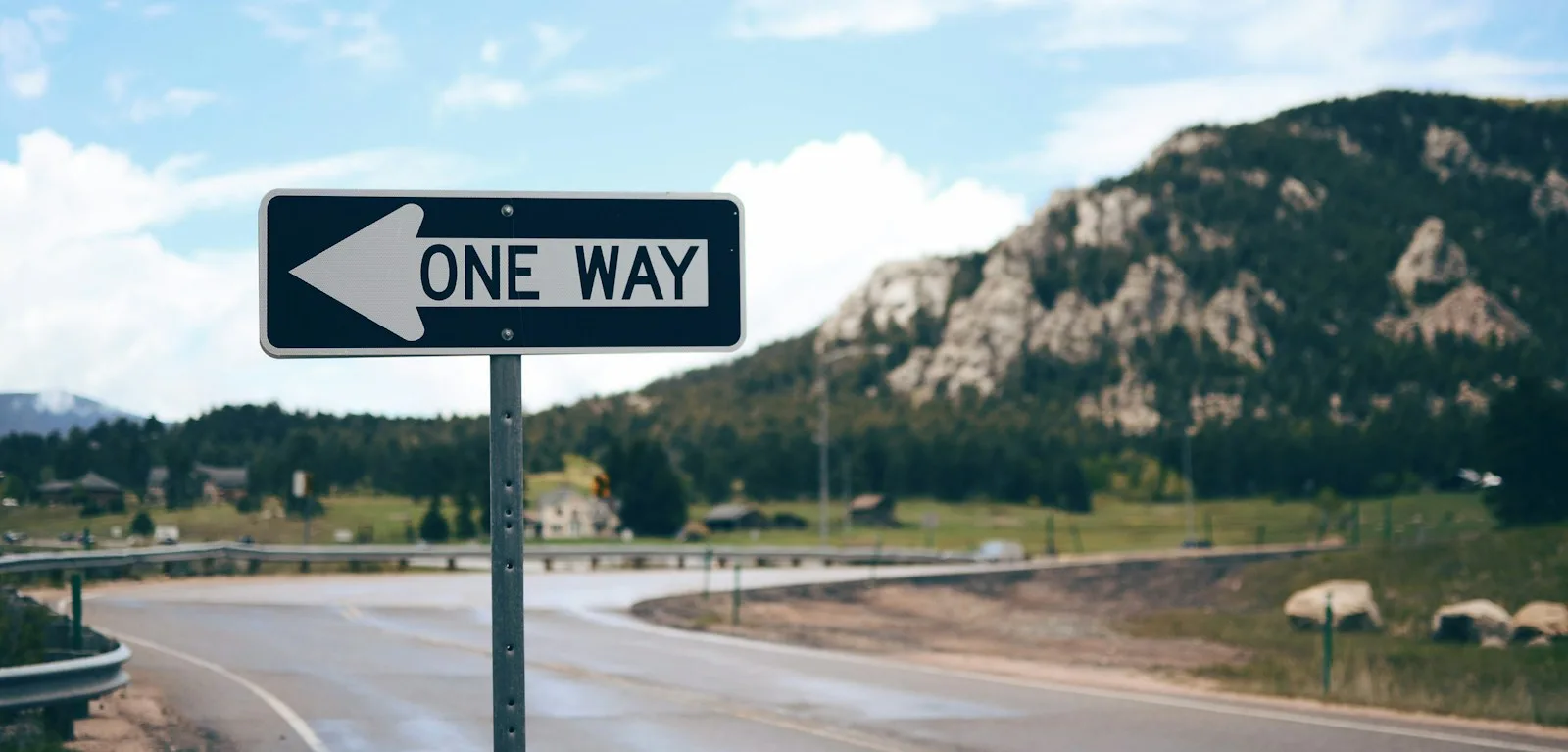 A one-way street sign beside a mountain road